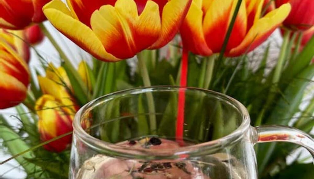 filiżanka z herbatą emotea na tle pomarańczowo-czerwonych tulipanów