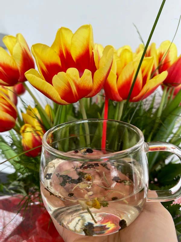 filiżanka z herbatą emotea na tle pomarańczowo-czerwonych tulipanów