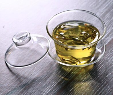 szklany gaiwan z zaparzoną zieloną herbatą z odłożoną pokrywką na stole