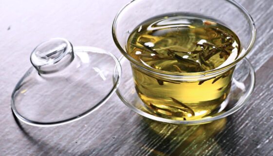 szklany gaiwan z zaparzoną zieloną herbatą z odłożoną pokrywką na stole