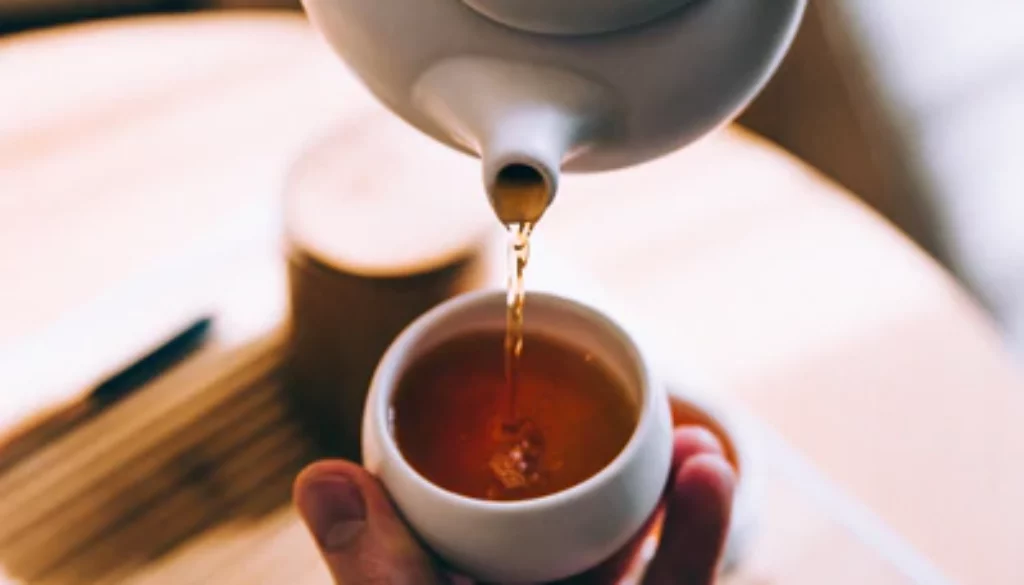 herbata emotea wlewana z białego czajniczka do białej czarki trzymanej w dłoni